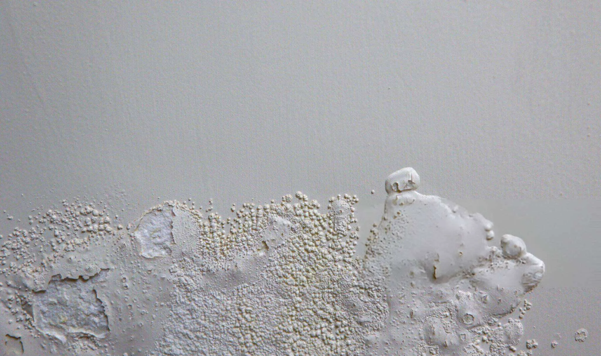 Close-up of a plaster wall with water damage, showing bubbling and peeling paint.