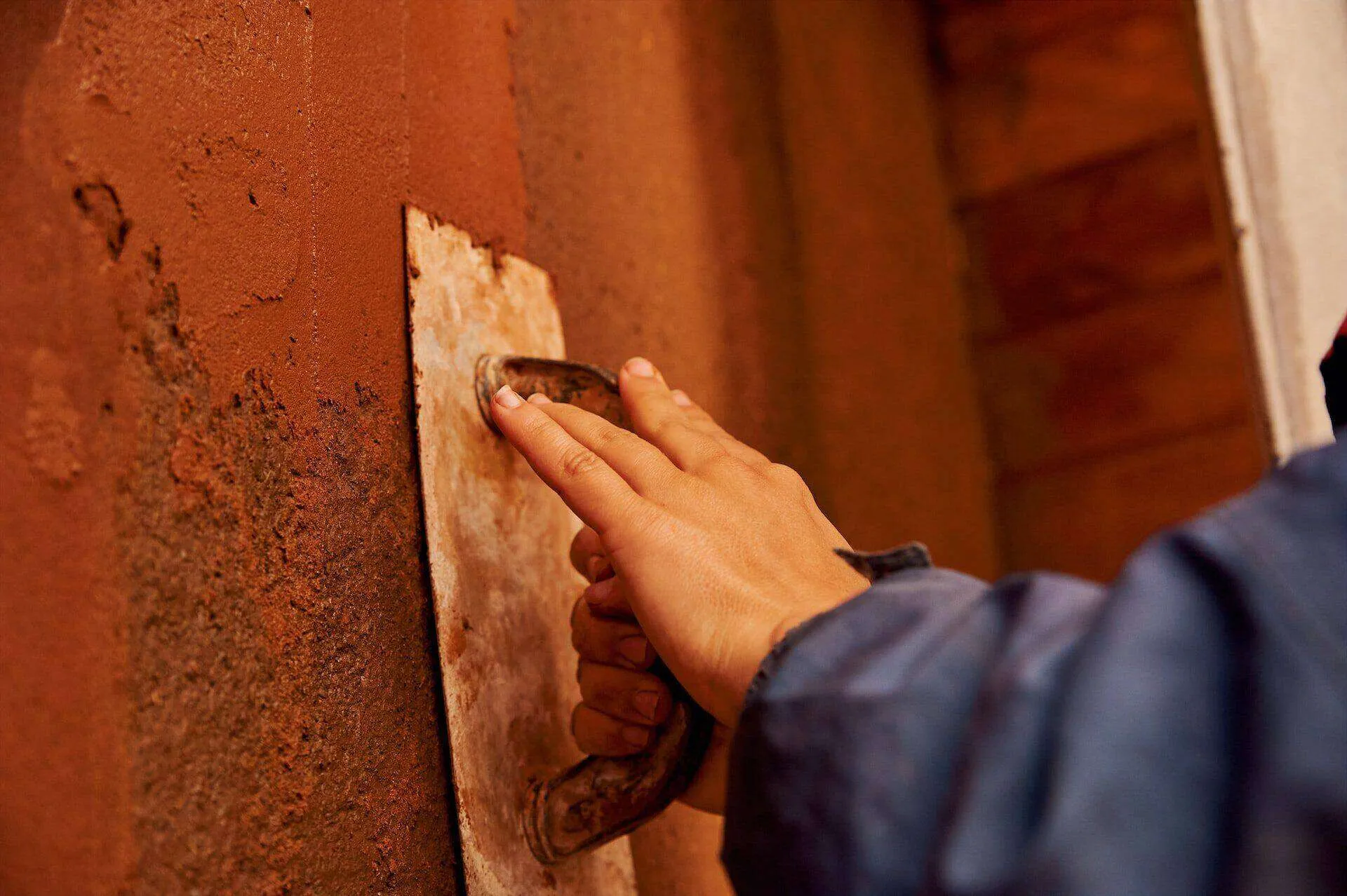 Close-up of a hand using a trowel to apply plaster on a wall.