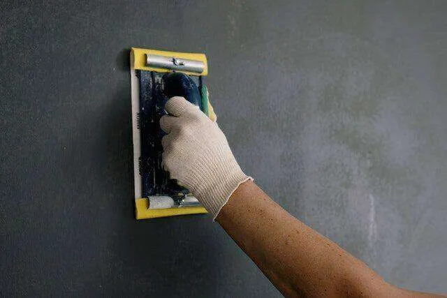 Person smoothing a plastered wall with a trowel, wearing a glove.