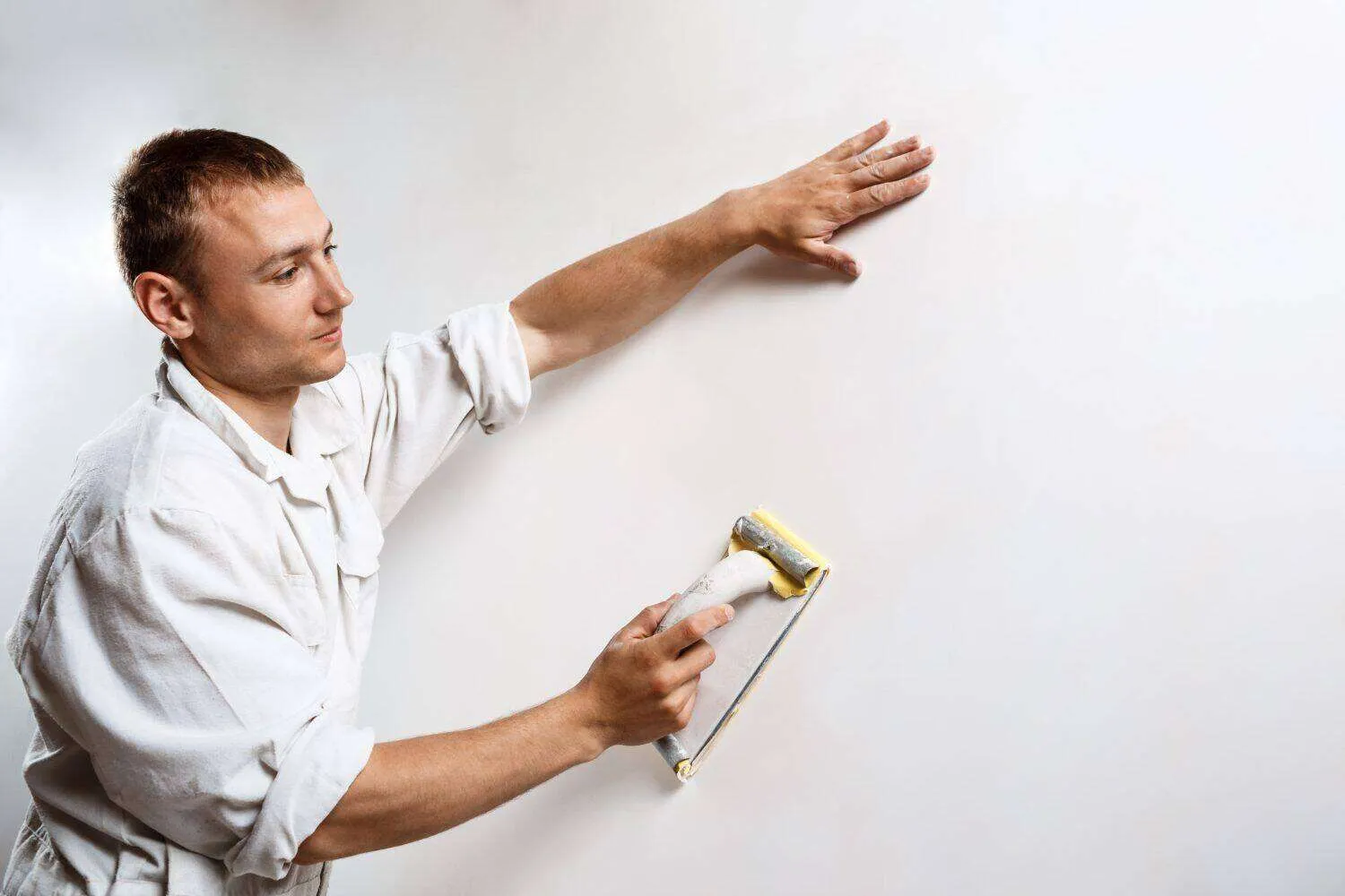 Person smoothing a plastered wall with a tool, wearing a white outfit.