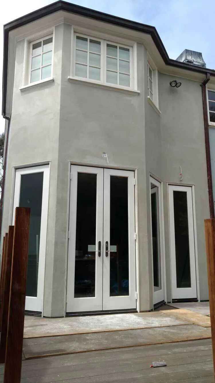 Corner of a house with smooth stucco finish, windows, and double doors leading to a deck. — El Cerrito area