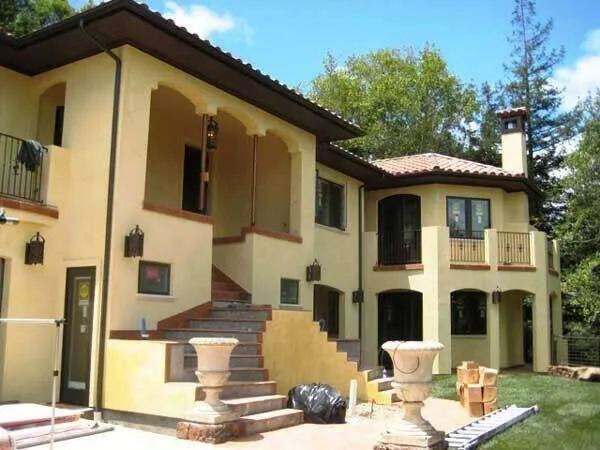 Two-story home with yellow stucco exterior, red-tiled roof, and arched windows.