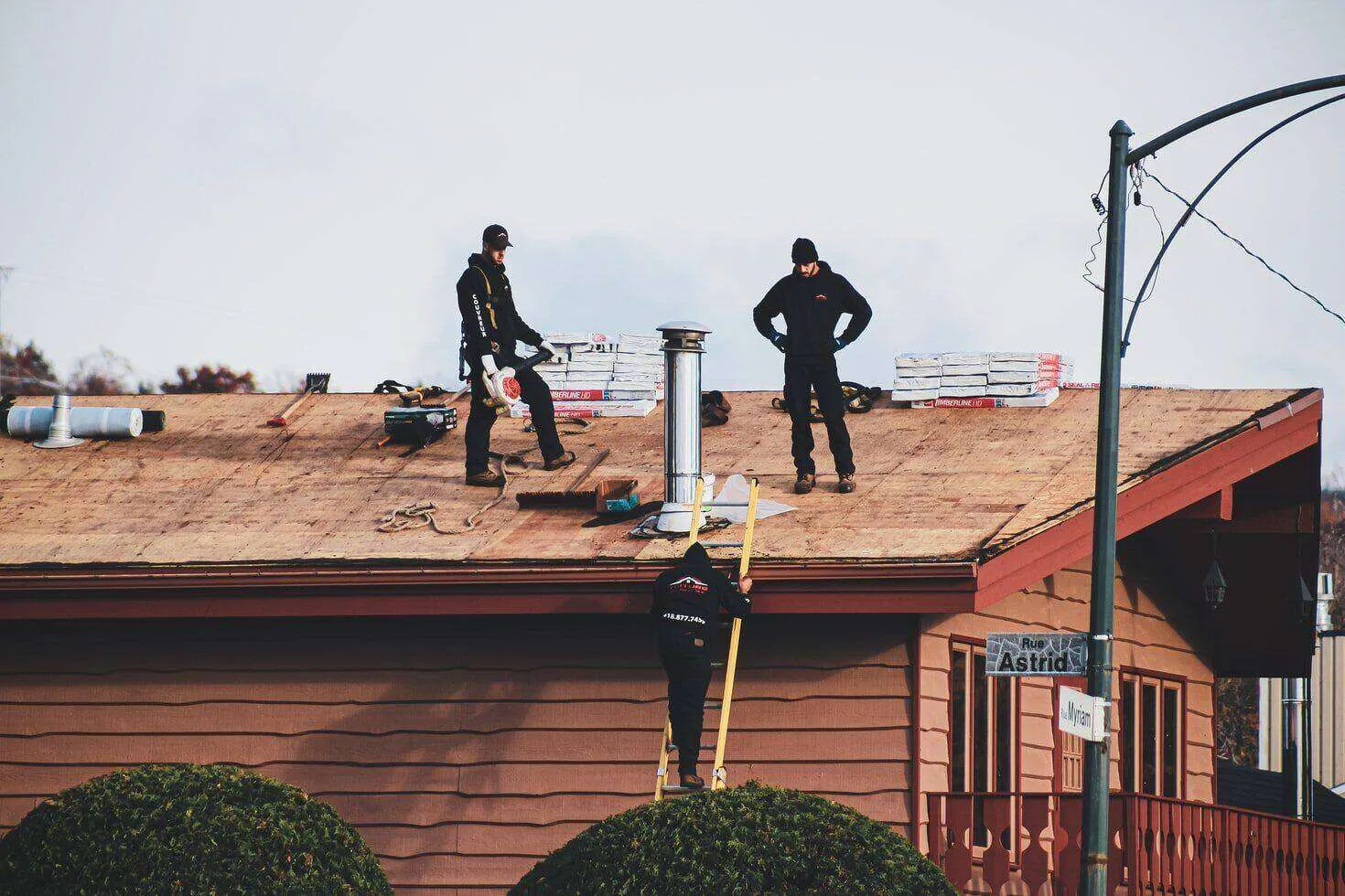 Three men working on a house roof with construction materials and tools visible.