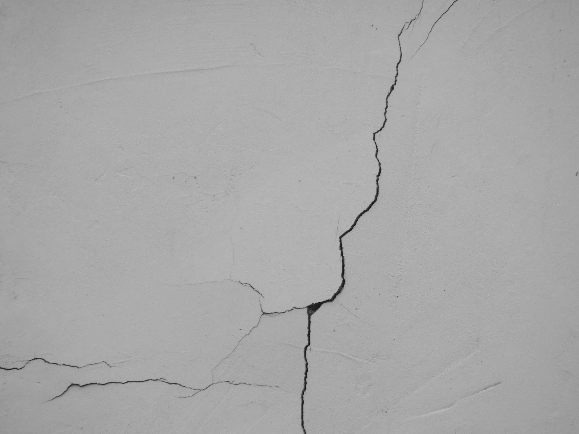Close-up of a vertical settlement crack on a smooth plaster wall surface.