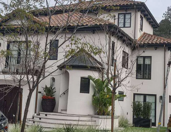 Two-story home with smooth acrylic stucco finish, tiled roof, and landscaped entrance.