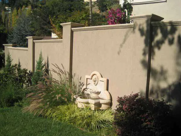 Smooth concrete plaster wall with decorative elements and landscaping in an exterior setting.