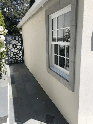 Exterior wall with smooth stucco finish and stone-trimmed window, adjacent to a stone-tiled walkway. — work near Kensington