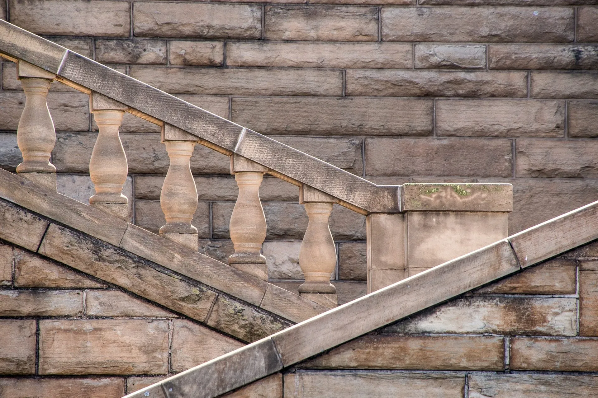 Close-up of a stone railing with balusters on a staircase against a stone wall.