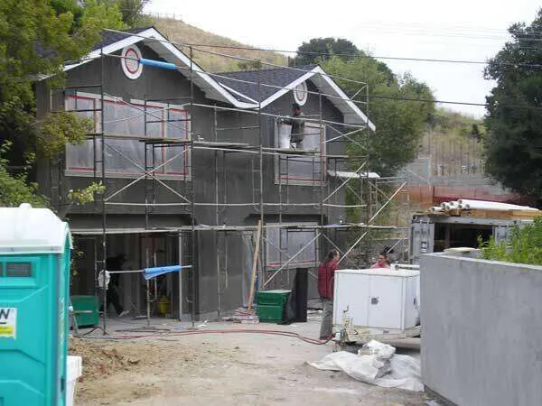 Two-story house with scaffolding and workers applying stucco to the exterior walls. — Greenbrae area
