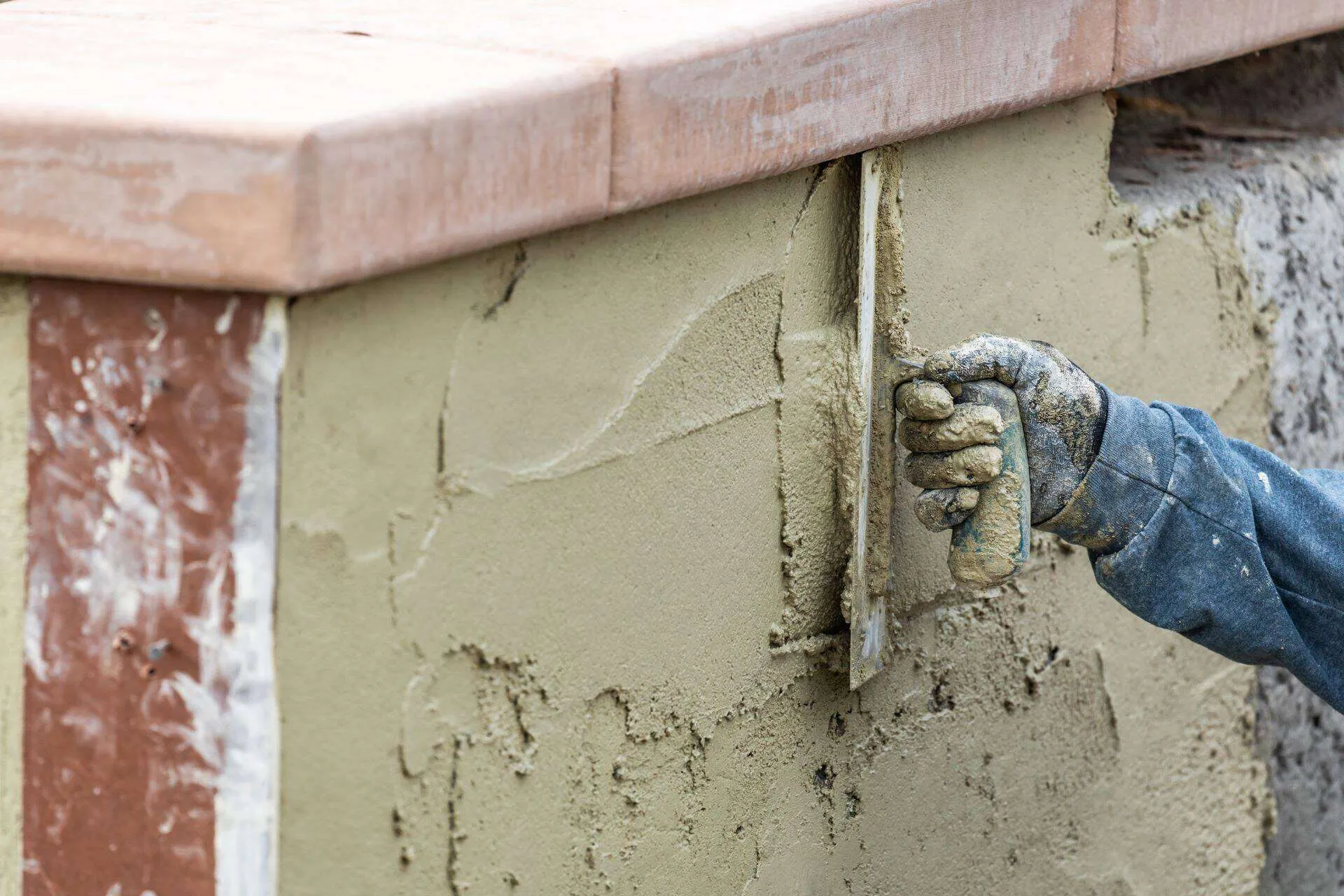 Worker applying stucco to a wall with a trowel, showing construction process.
