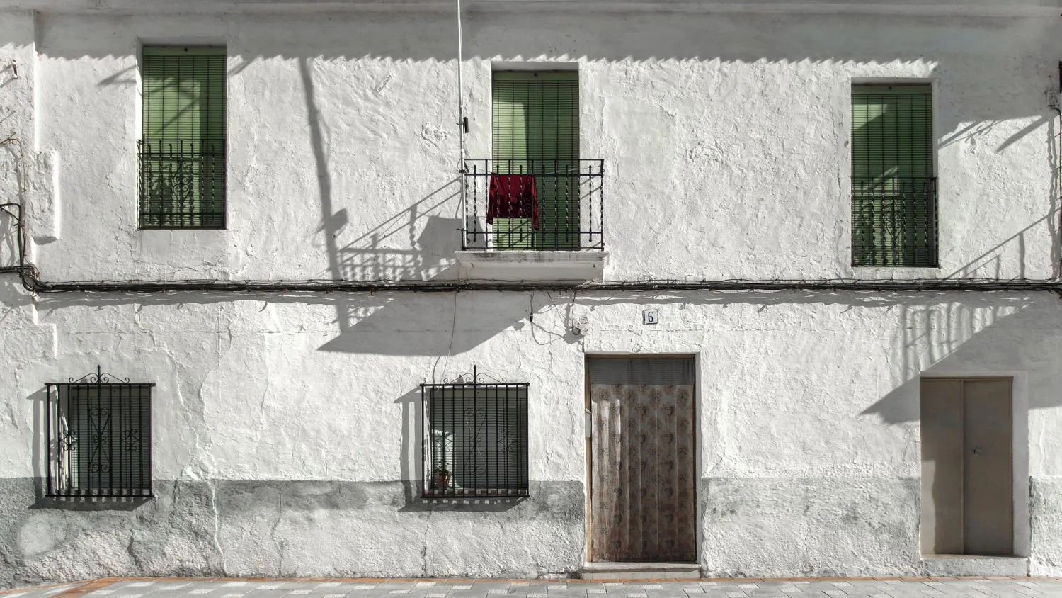 White stucco building with green shutters and metal railings, showing textured finish.
