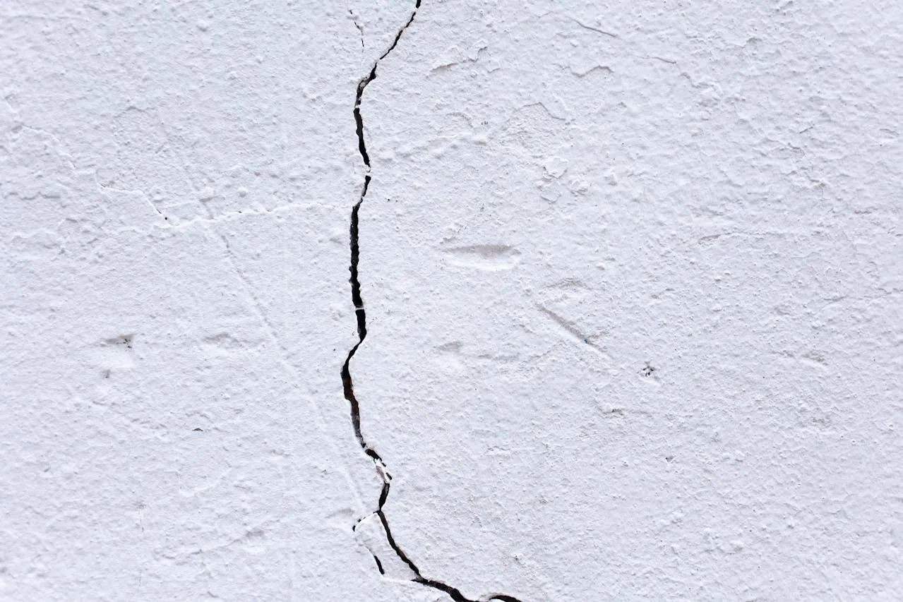 Close-up of a vertical crack in a white stucco wall showing texture.