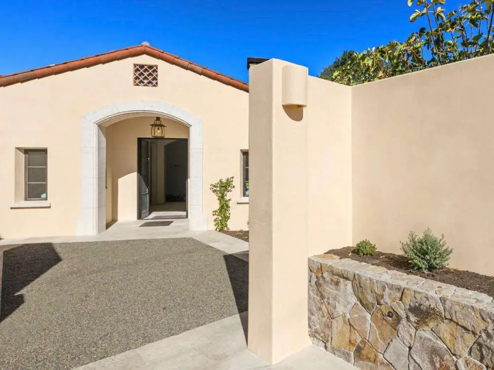 Stucco building exterior with arched entrance and stone wall planter under clear blue sky. — work near Napa