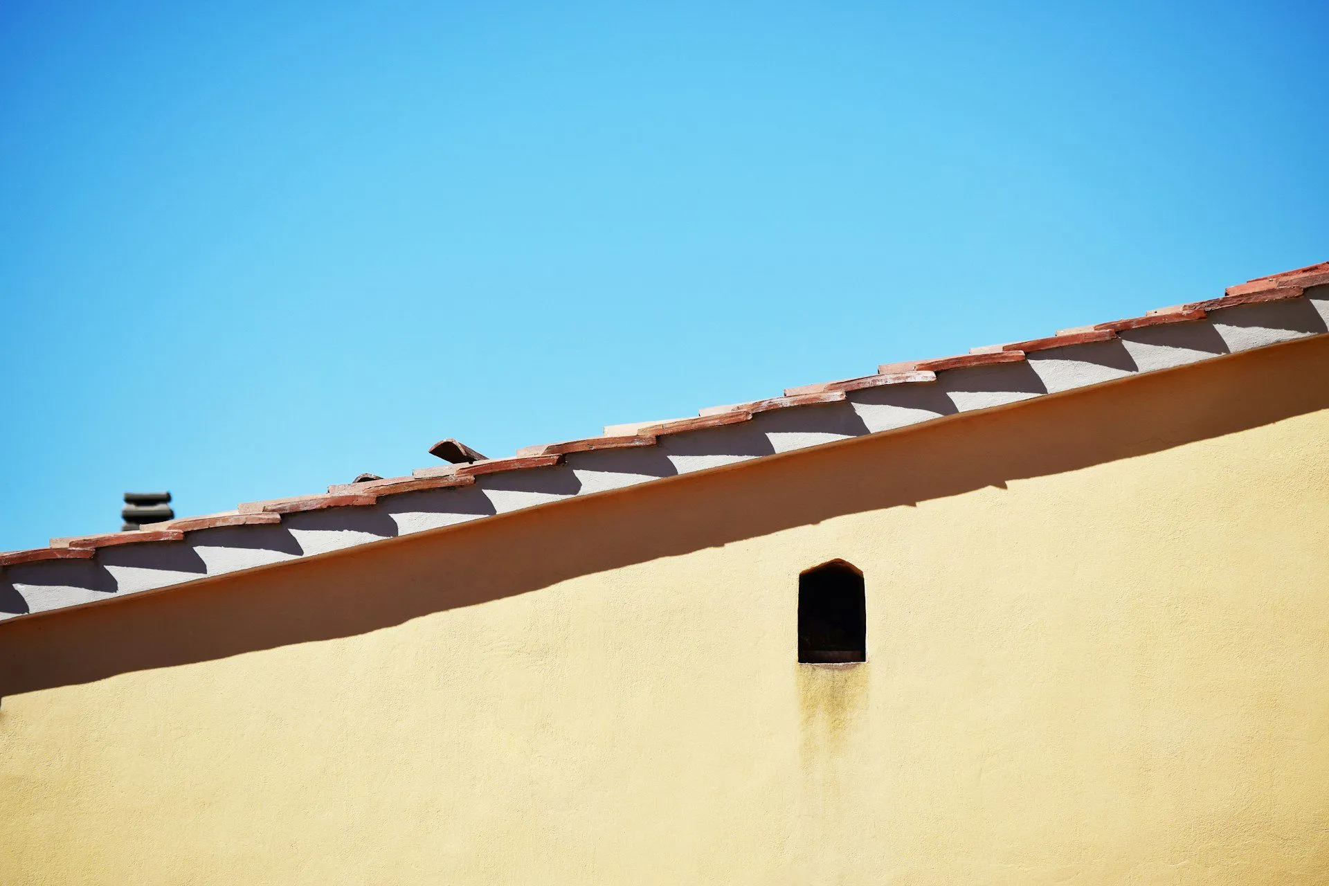 Yellow stucco wall with sloped roof and small vent under a clear blue sky. — Alameda area