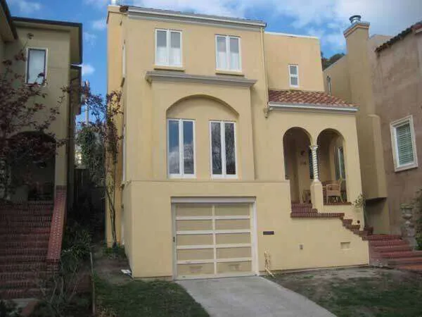 Two-story house with stucco finish, garage, and porch with brick stairs.