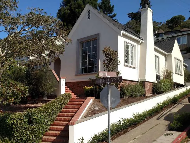 White stucco house with brick foundation and chimney on a corner lot in Mill Valley.