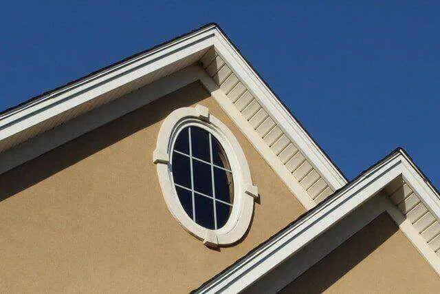 Stucco house section with oval window and white trim under a blue sky. — Kentfield area