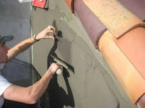 Worker applying stucco over mesh on exterior wall near terracotta roof tiles. — San Rafael area