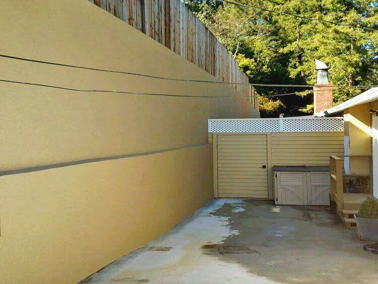 Smooth stucco retaining wall with wooden fence above, next to a driveway in Mill Valley. — work near Mill Valley