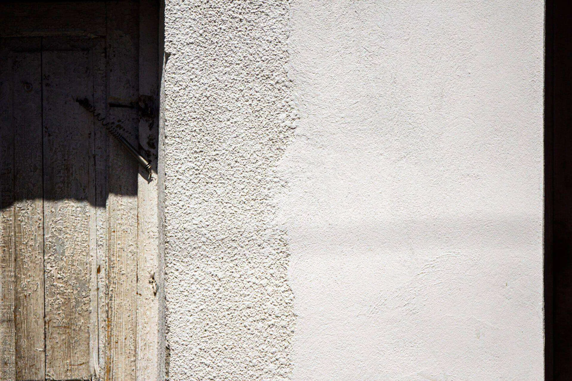 Close-up of a textured stucco wall next to a weathered wooden door, highlighting texture contrast.