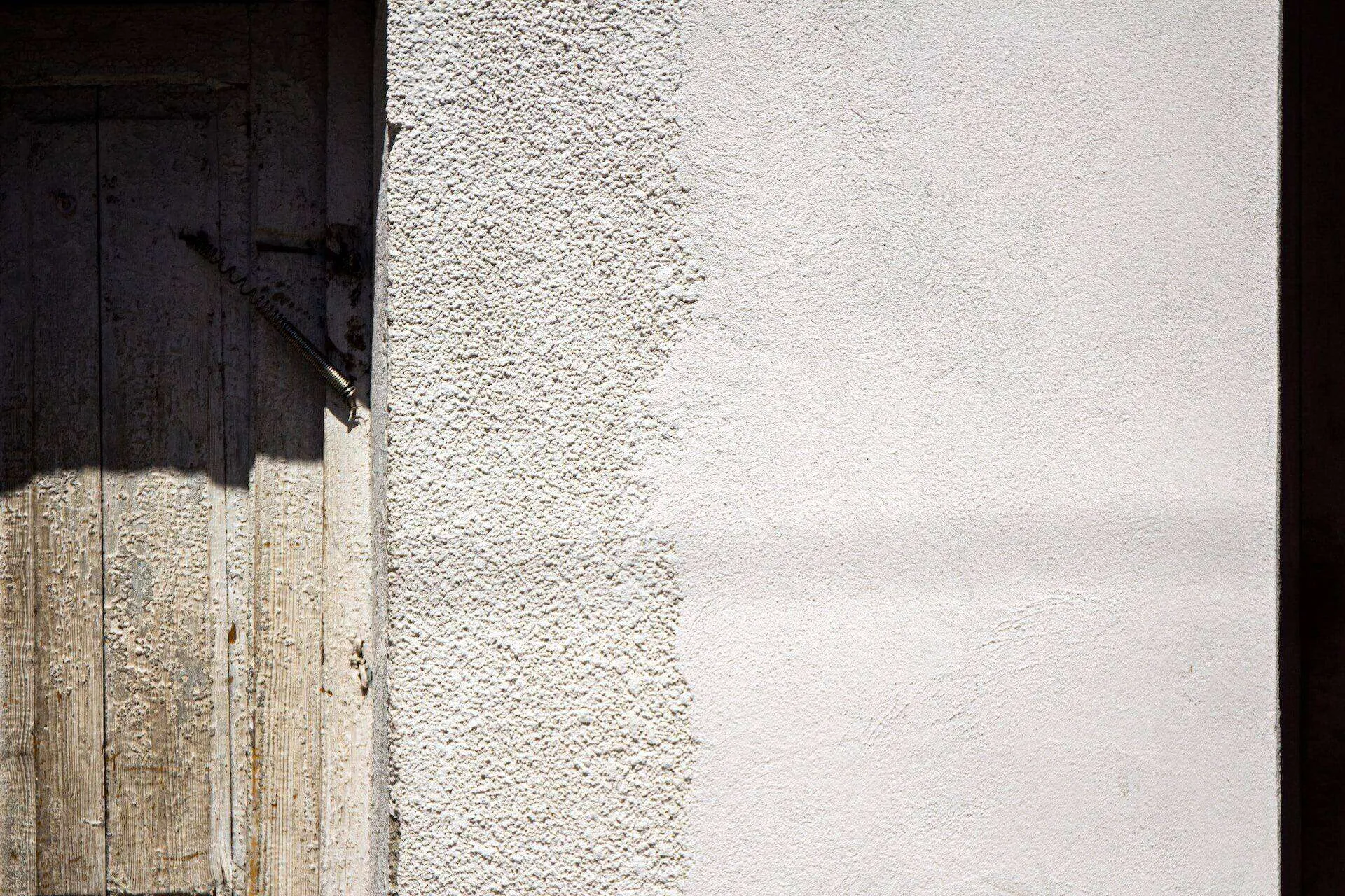 Close-up of a textured stucco wall beside a weathered wooden door in sunlight. — Larkspur area