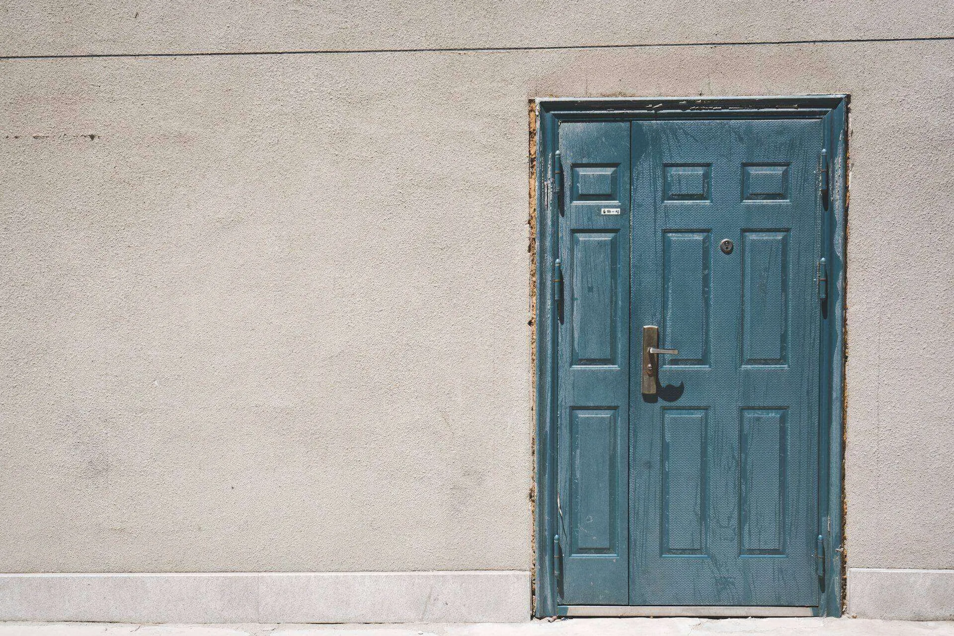 Blue double door set in a plain stucco wall, showing signs of wear. — Berkeley area