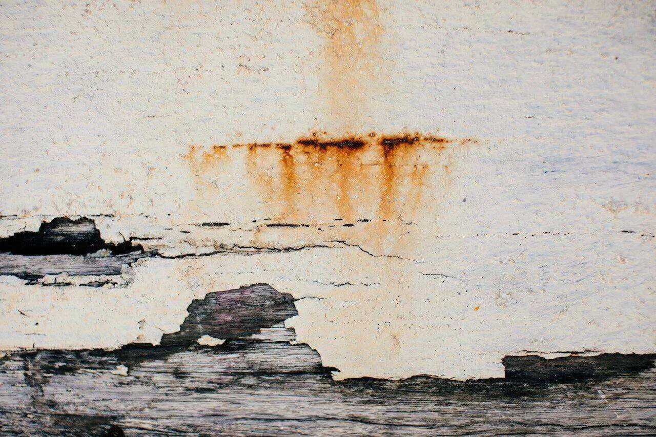 Close-up of a stucco wall showing water damage and rust stains, with visible cracks and deterioration.