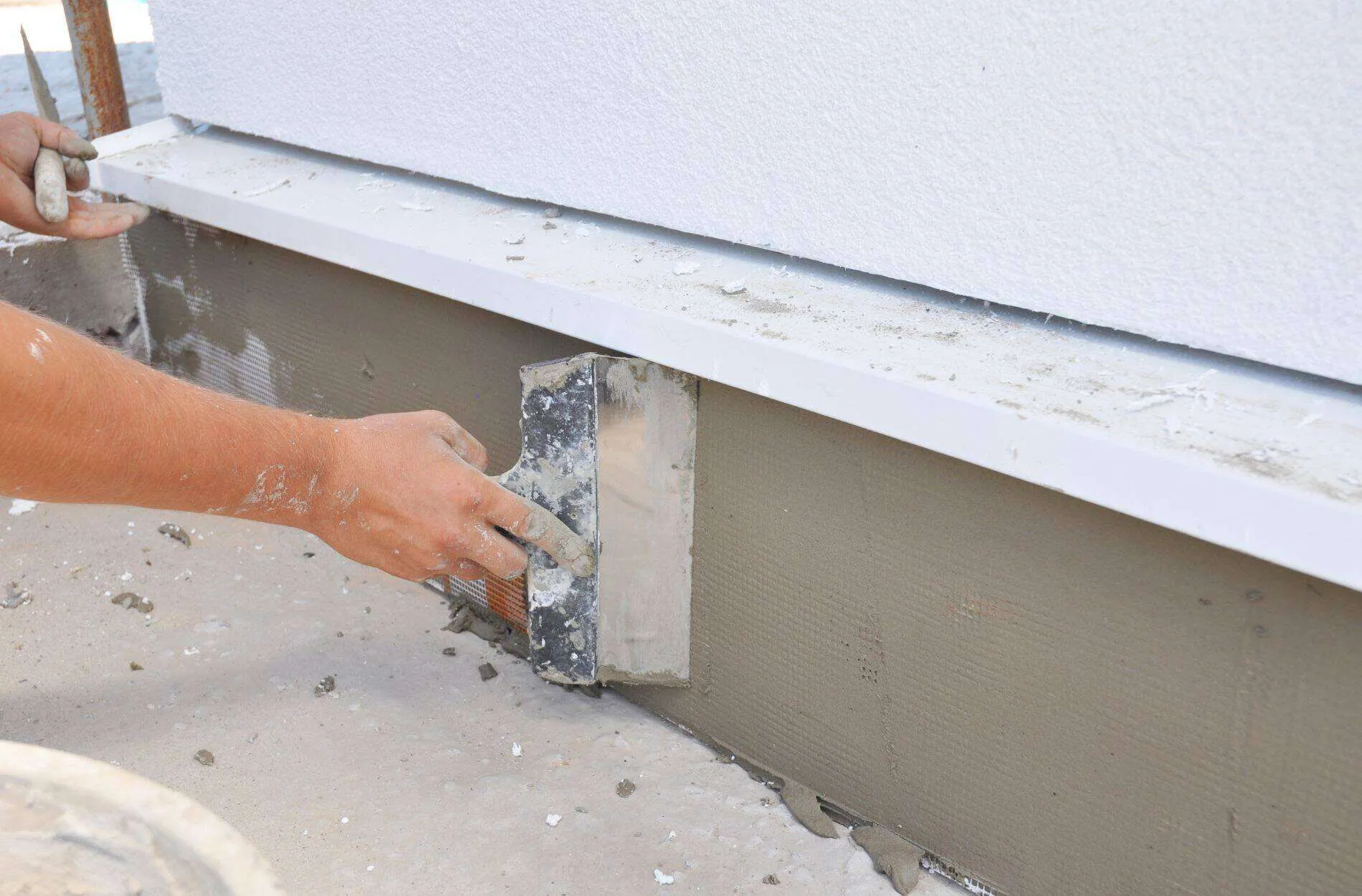Close-up of hands applying plaster for waterproofing on a wall base.