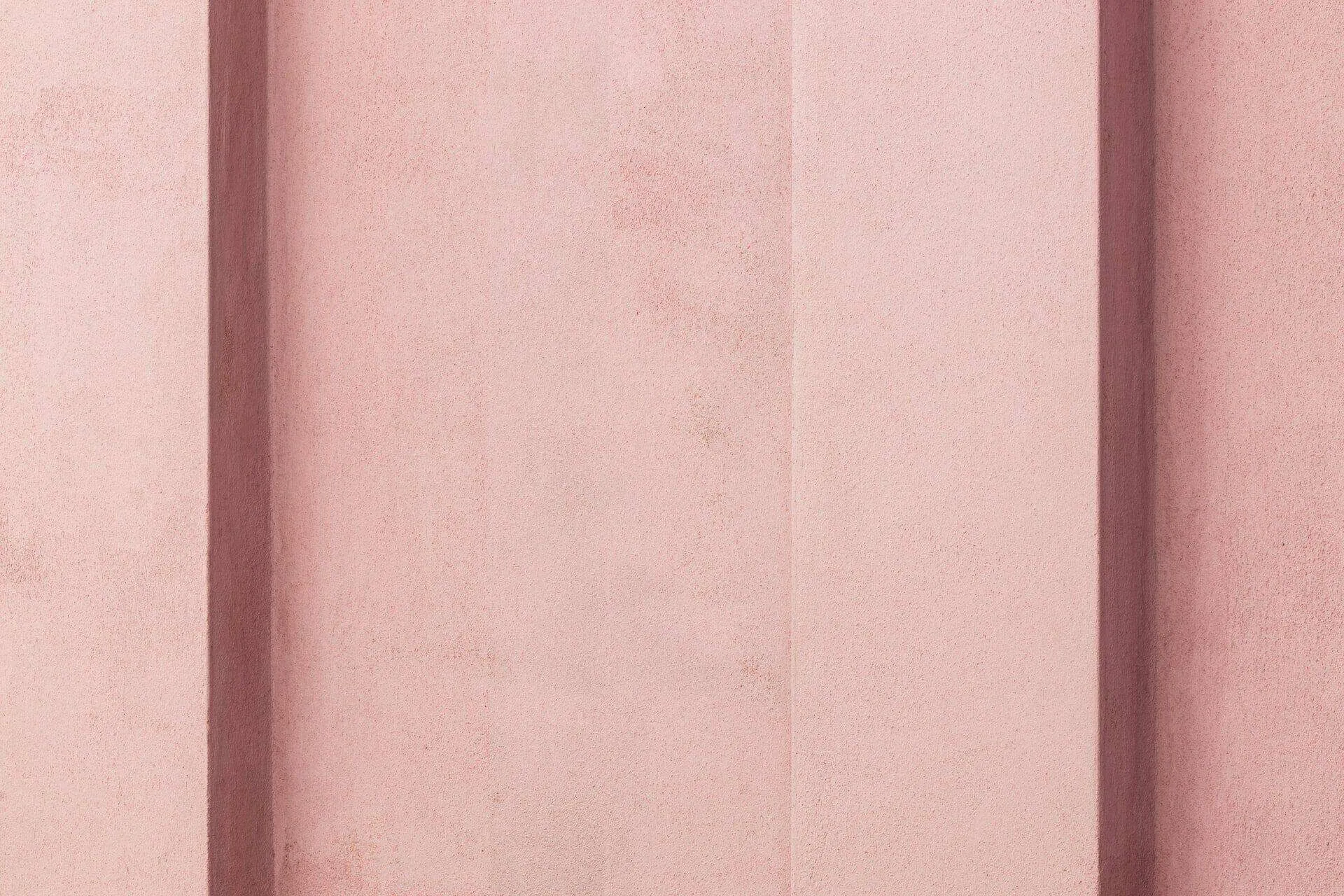 Close-up of a pink stucco wall with vertical grooves, showing texture and depth.