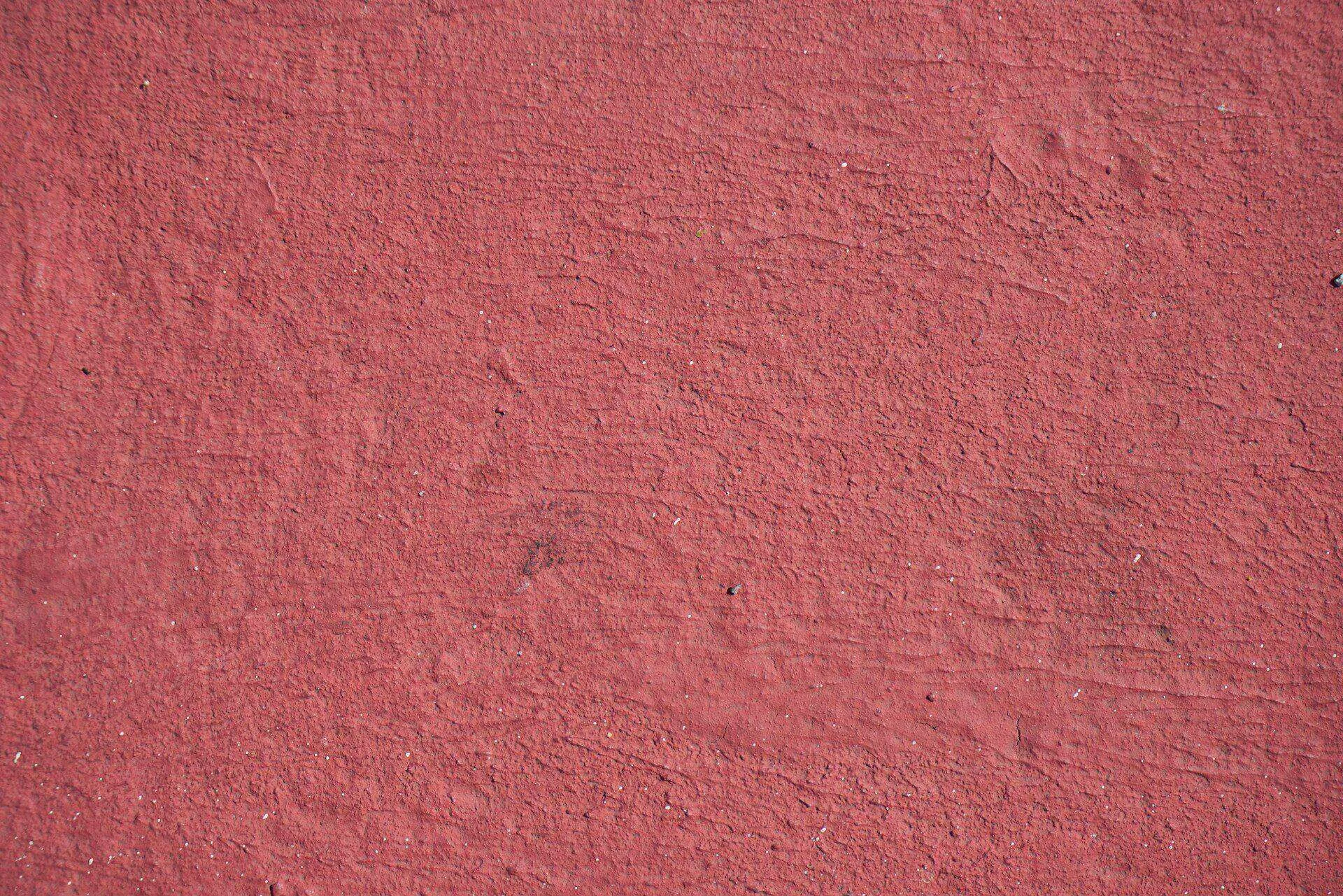 Close-up of a textured red plaster wall with a rough finish and visible imperfections.