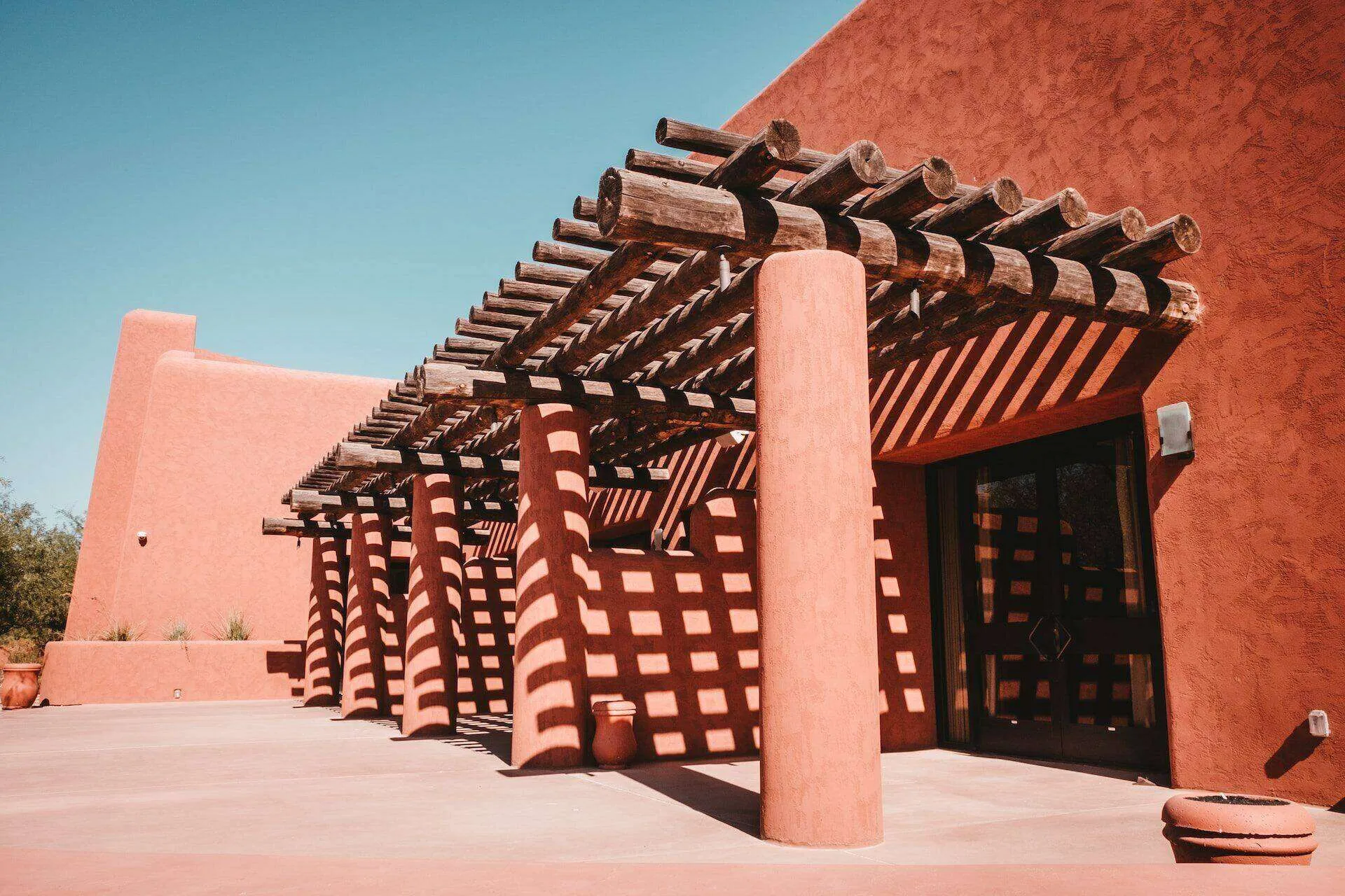 Building with terracotta stucco finish and wooden pergola casting shadows on the patio.