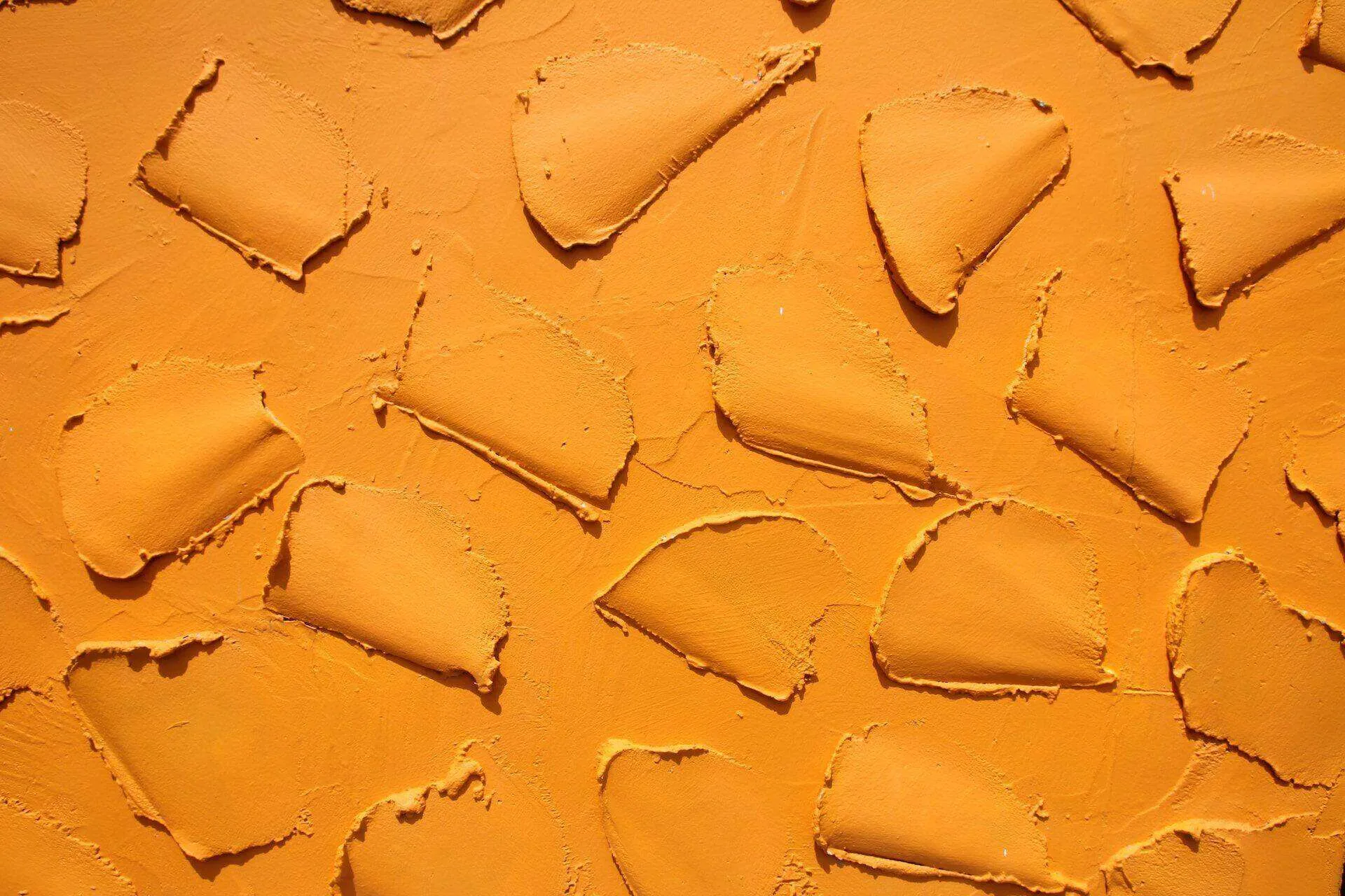 Close-up of a textured wall with orange Venetian plaster finish, showing overlapping smooth patches.