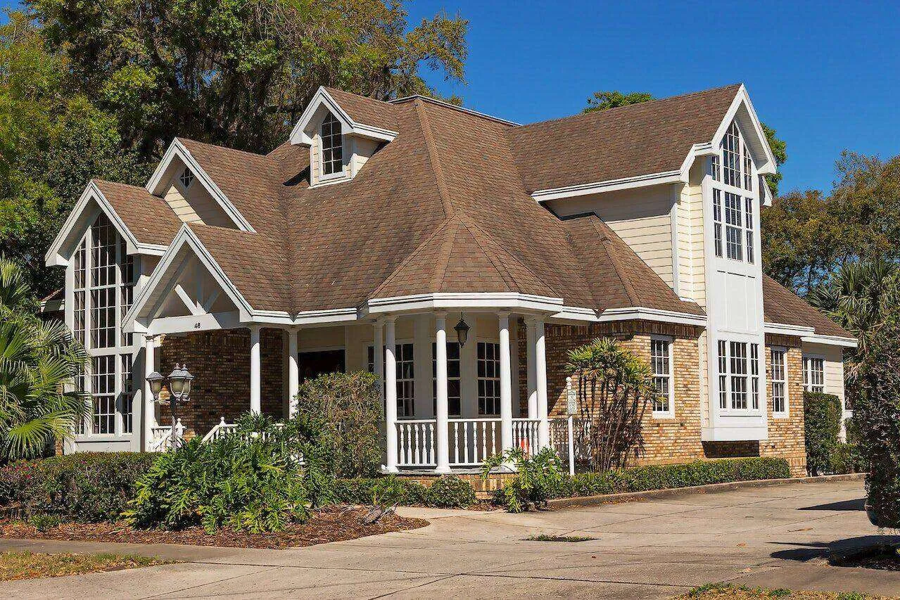 Large traditional home with brick and siding, multiple gables, and a porch surrounded by greenery.