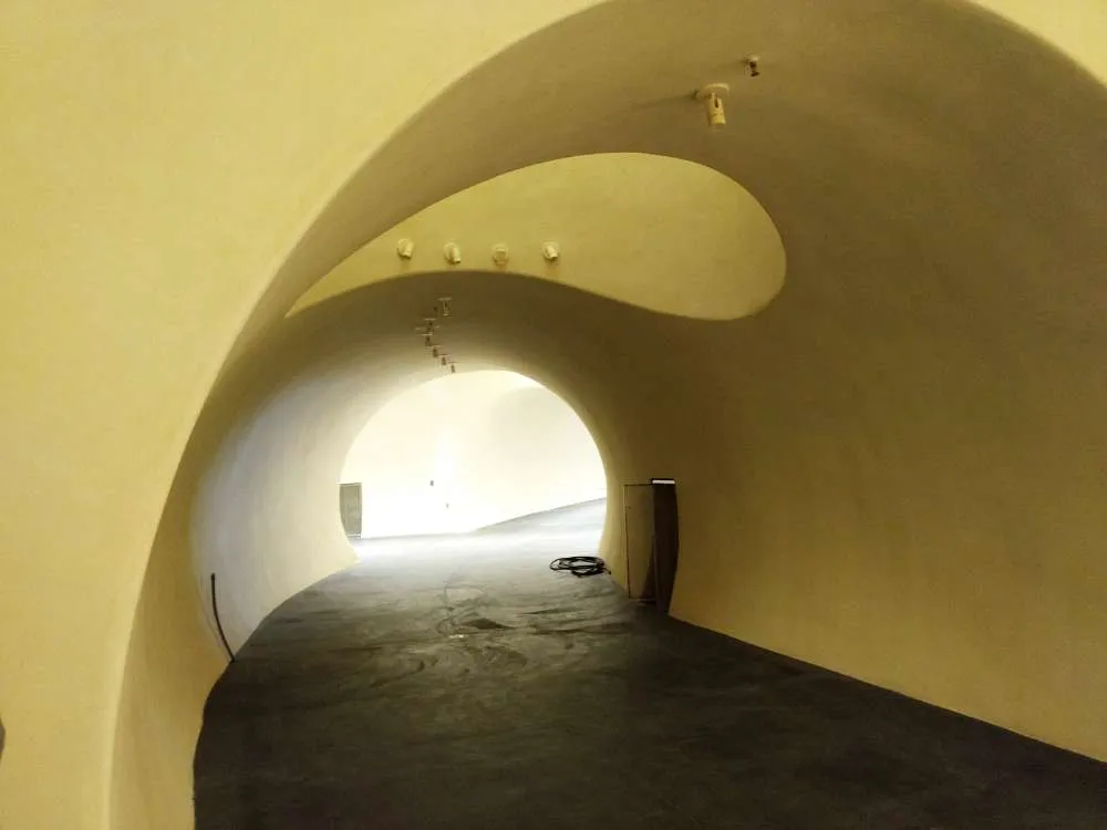 Curved interior of an underground wine cave with smooth beige walls and a dark floor.