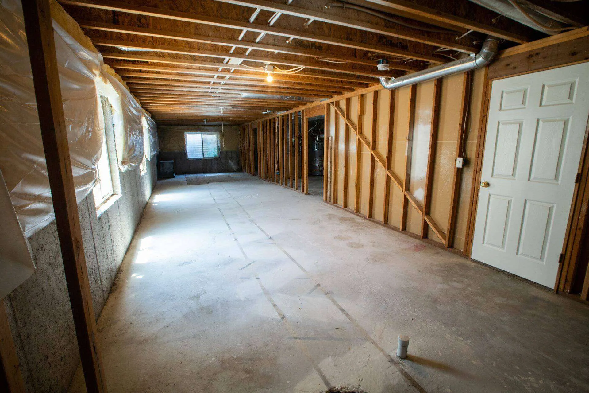 Unfinished basement with exposed beams, concrete floor, and plastic-covered windows.