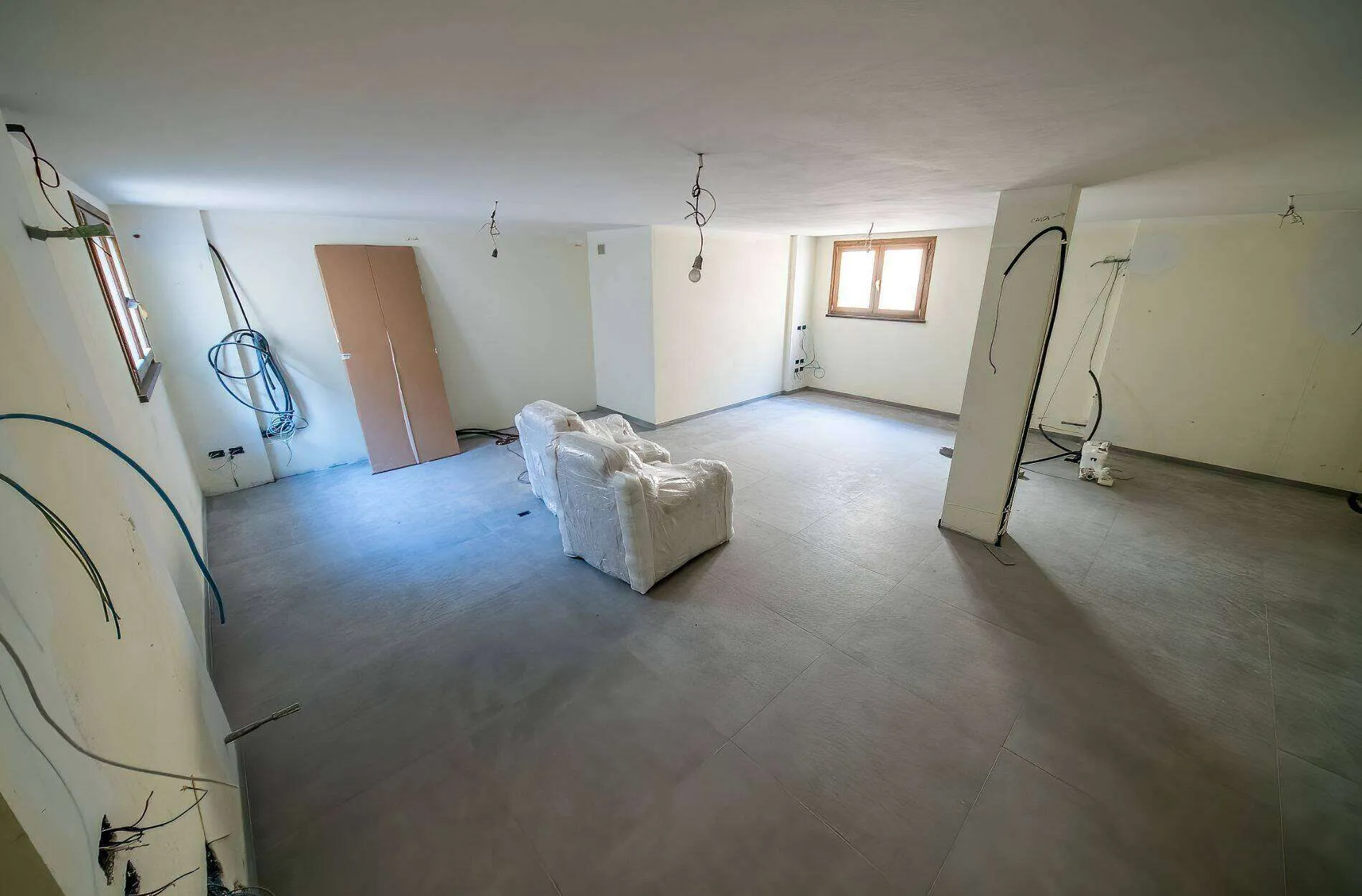 Unfinished basement with bare walls, exposed wires, and wrapped furniture.