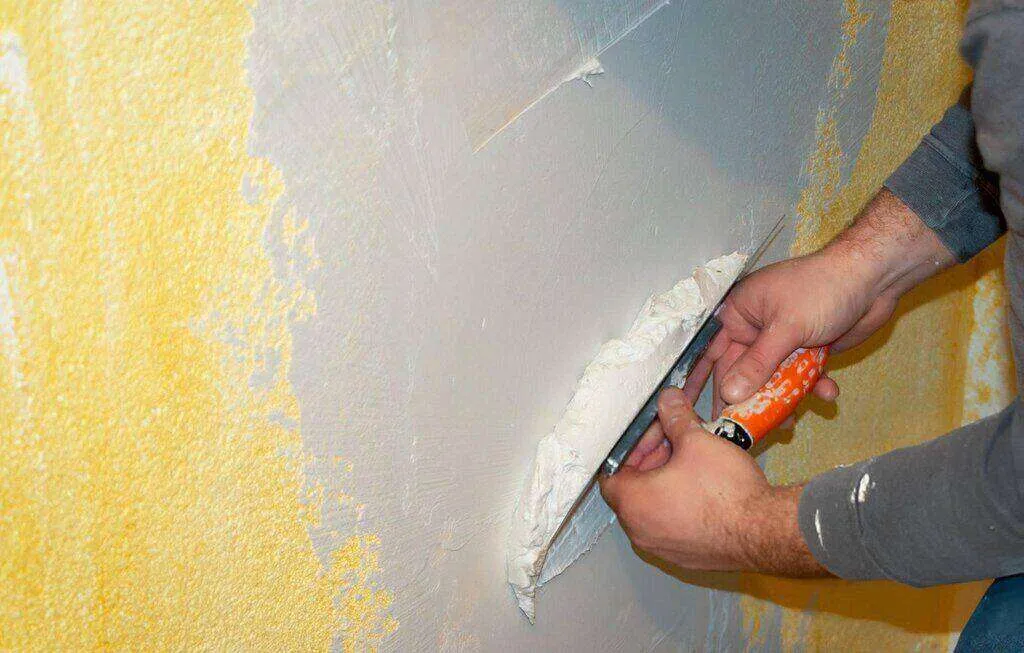 Person applying white plaster to a yellow wall with a trowel. — Richmond area
