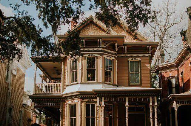 Victorian-style house with ornate wooden trim, covered porch, and multiple windows surrounded by trees.