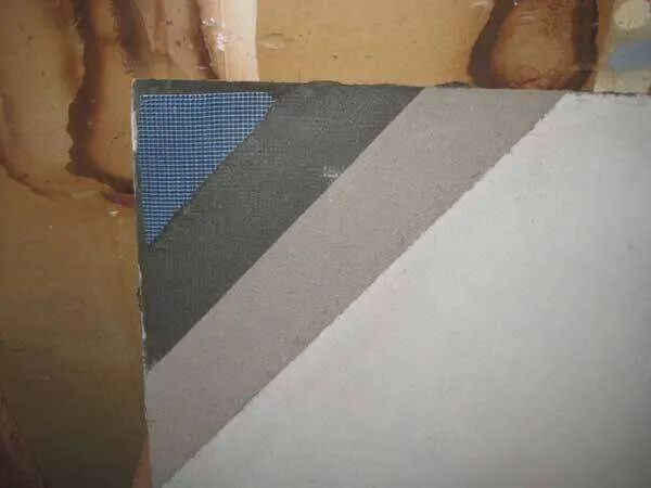 Close-up of a wall corner showing blue mesh and plaster layers.