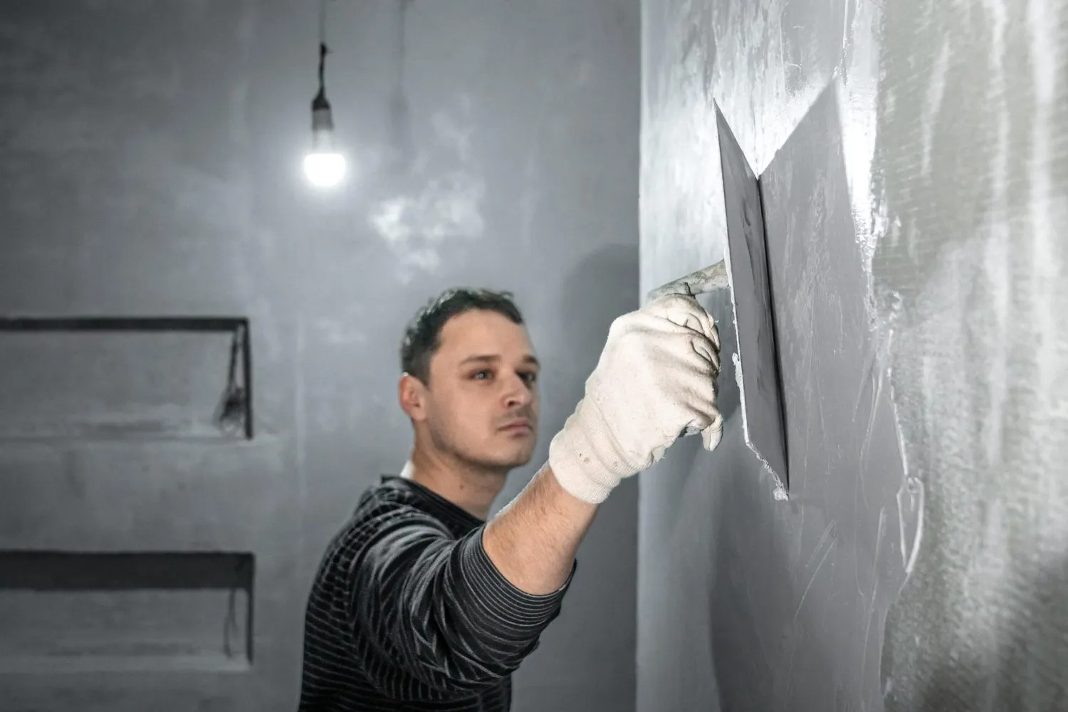 Person applying plaster to a wall with a trowel in a dimly lit room. — Corte Madera area