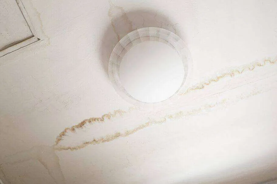 Ceiling with water stains and discoloration around a light fixture, indicating water damage.