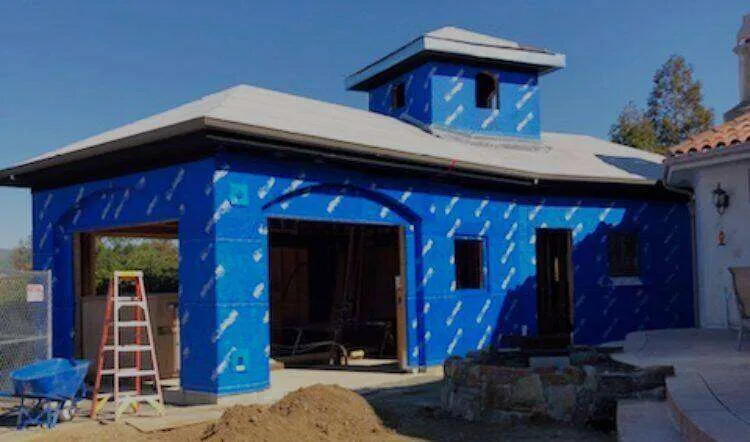 Building under construction with blue waterproofing membrane, ladder, and materials.