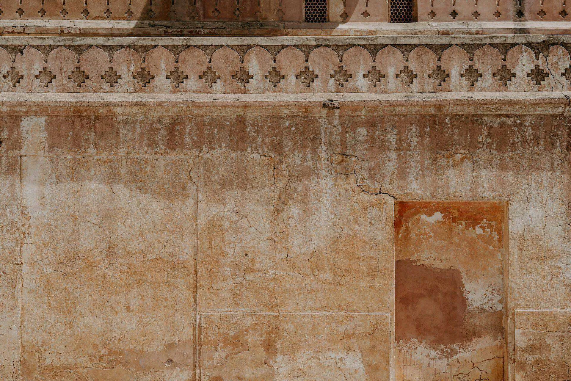 Aged plaster wall with cracks and an ornate decorative border at the top, showing signs of wear.
