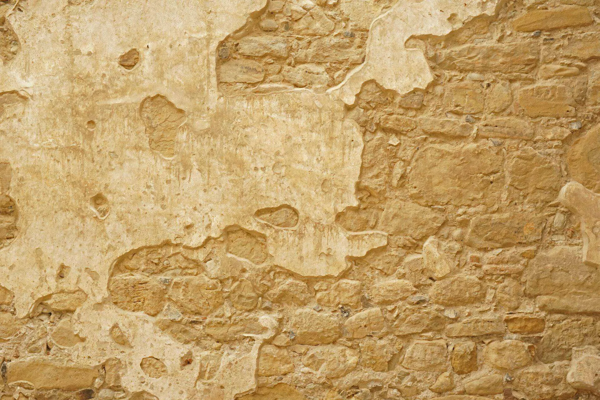 A weathered wall with missing stucco revealing the stone underneath, showing signs of aging and wear. — Berkeley area