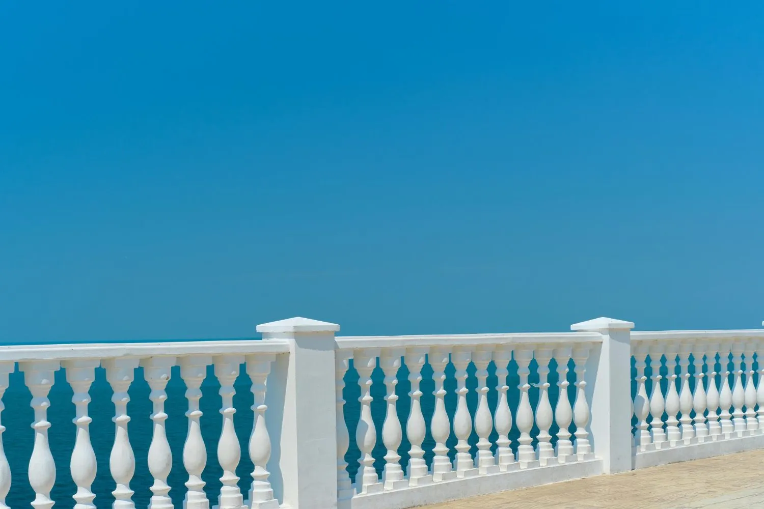 White stone railing with balusters against a blue sky and ocean backdrop.