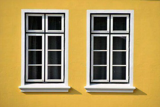 Two white-framed windows with foam trim on a bright yellow wall.
