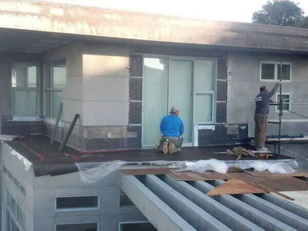Two workers patching windows on a building exterior with scaffolding and materials.