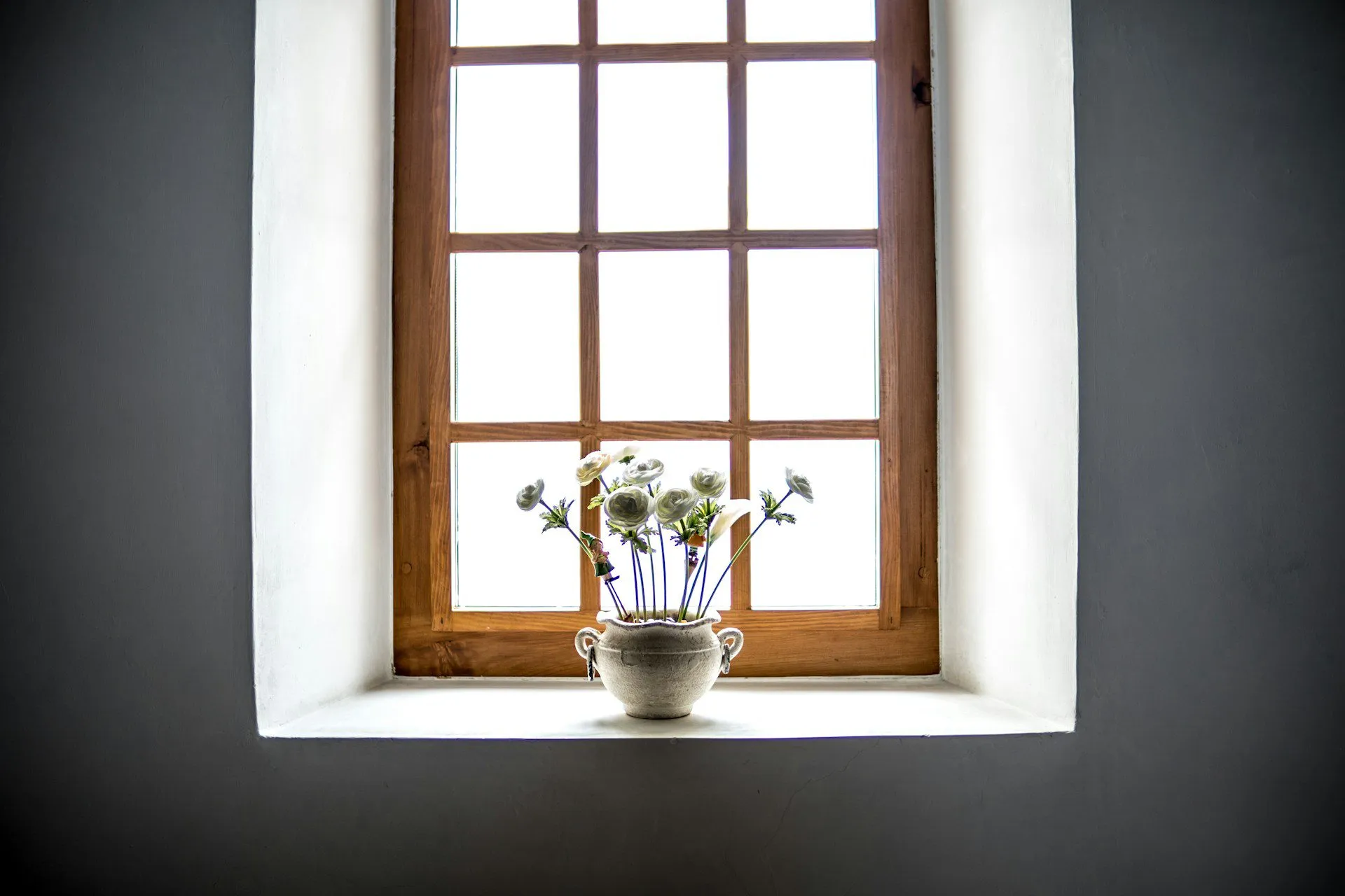 Wooden-framed window with multiple panes and a vase of flowers on the sill.